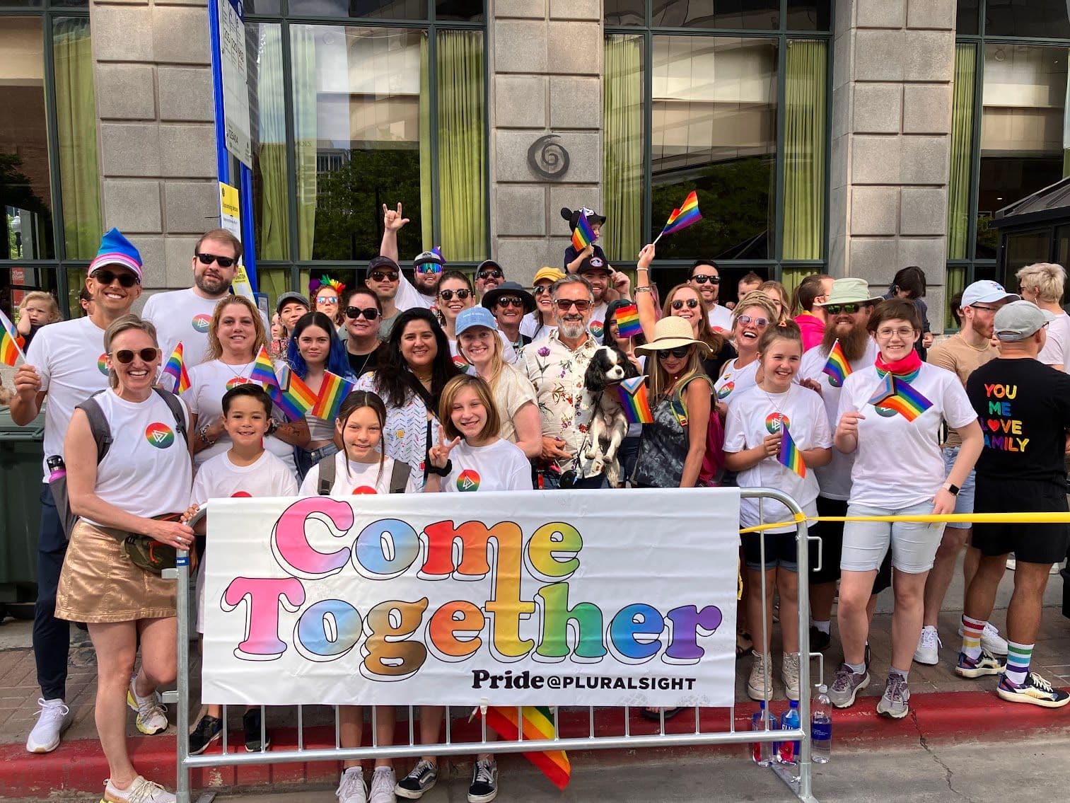Group photo at Salt Lake City Pride Parade showing diverse participants wearing rainbow colors and holding a 'Come Together Pride@PLURALSIGHT' banner, representing tech industry support for the LGBTQ+ community.