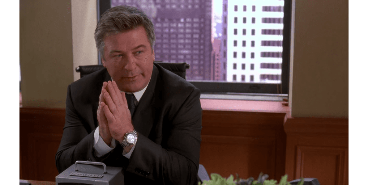 Jack Donaghy from 30 Rock in his executive office, wearing a dark suit and tie, sitting at his desk with hands pressed together thoughtfully against a Manhattan skyline backdrop.